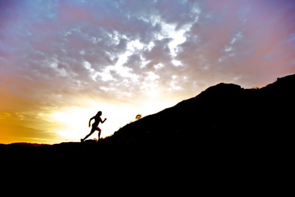 Runner in silhouette against rising sun, running uphill